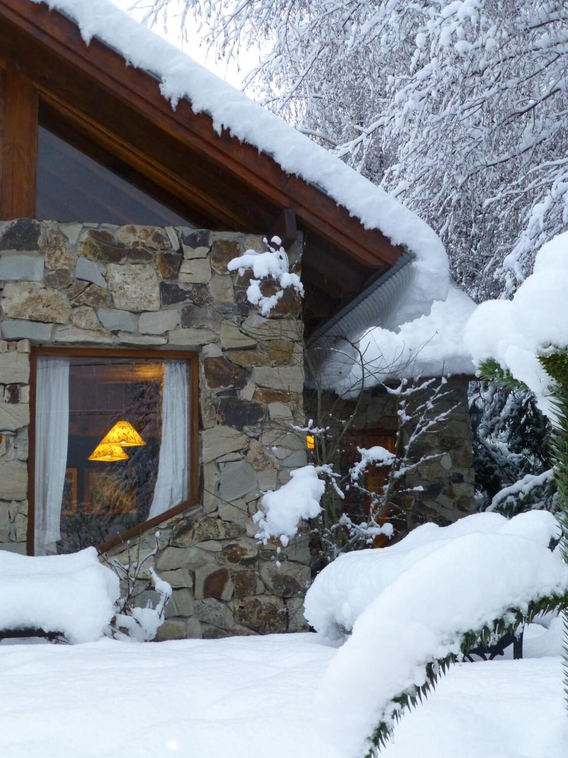 Ventana iluminada en la pared de piedra, con nieve en el techo